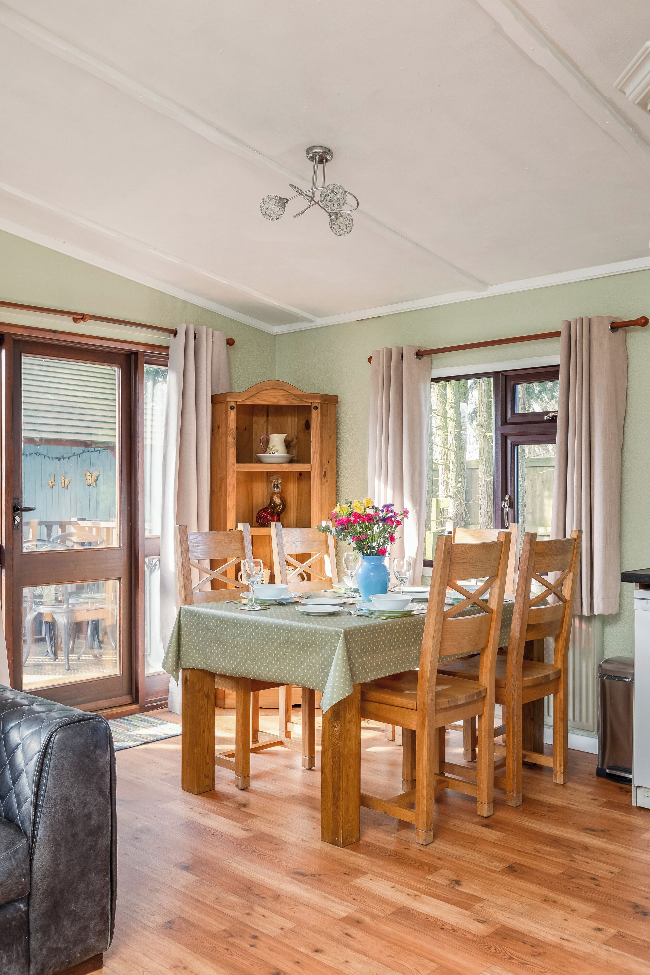 Un comedor con una mesa de madera dispuesta para cuatro, rodeada de sillas de madera. Se ve un aparador de madera con vajilla al fondo.