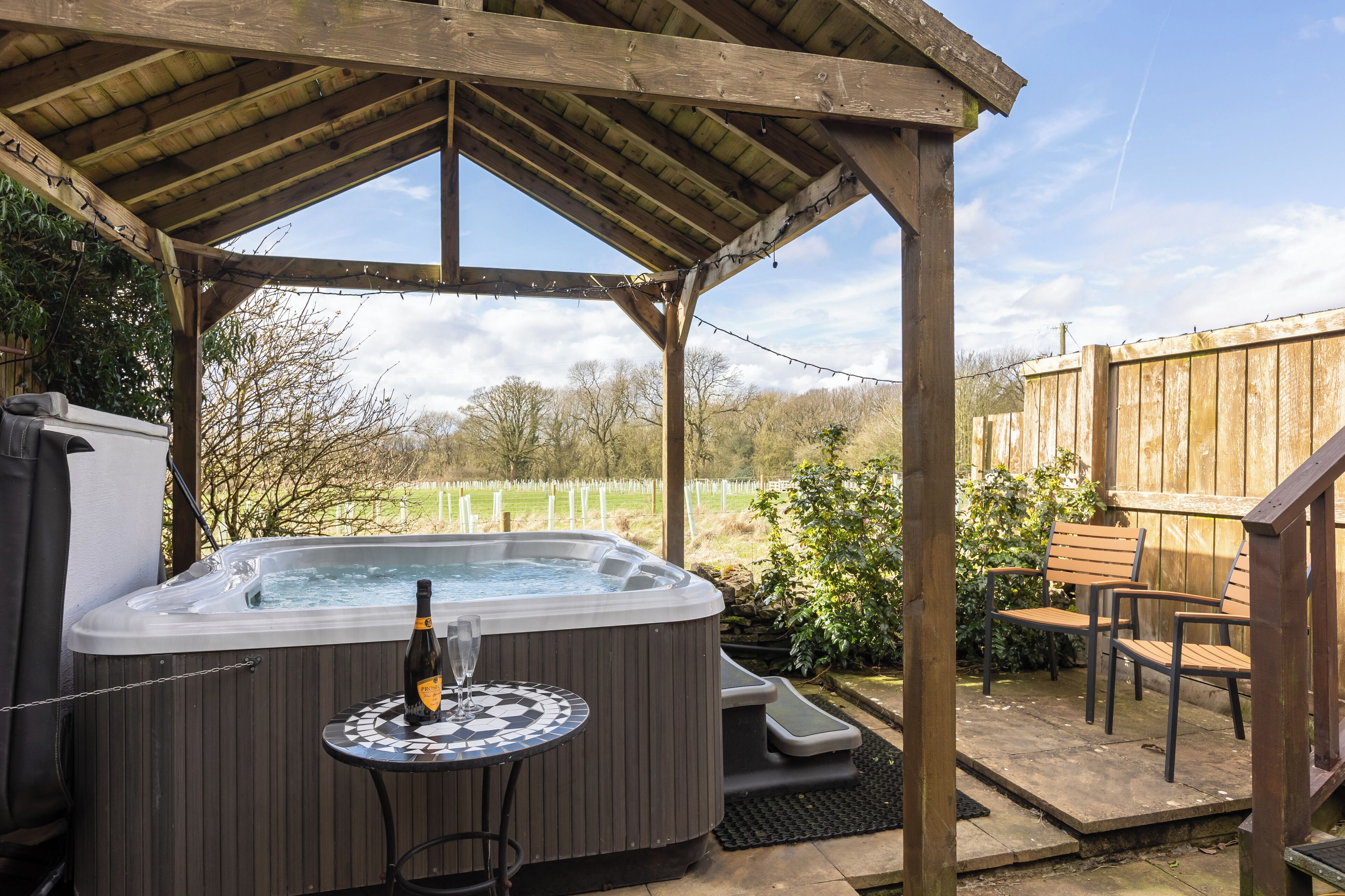 A hot tub under a wooden pergola with a table and chairs nearby.