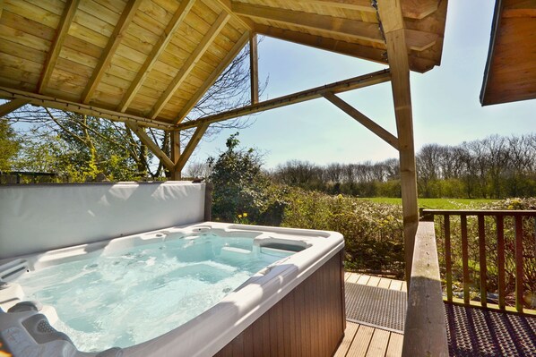 A hot tub on a wooden deck with a wooden pergola overhead.