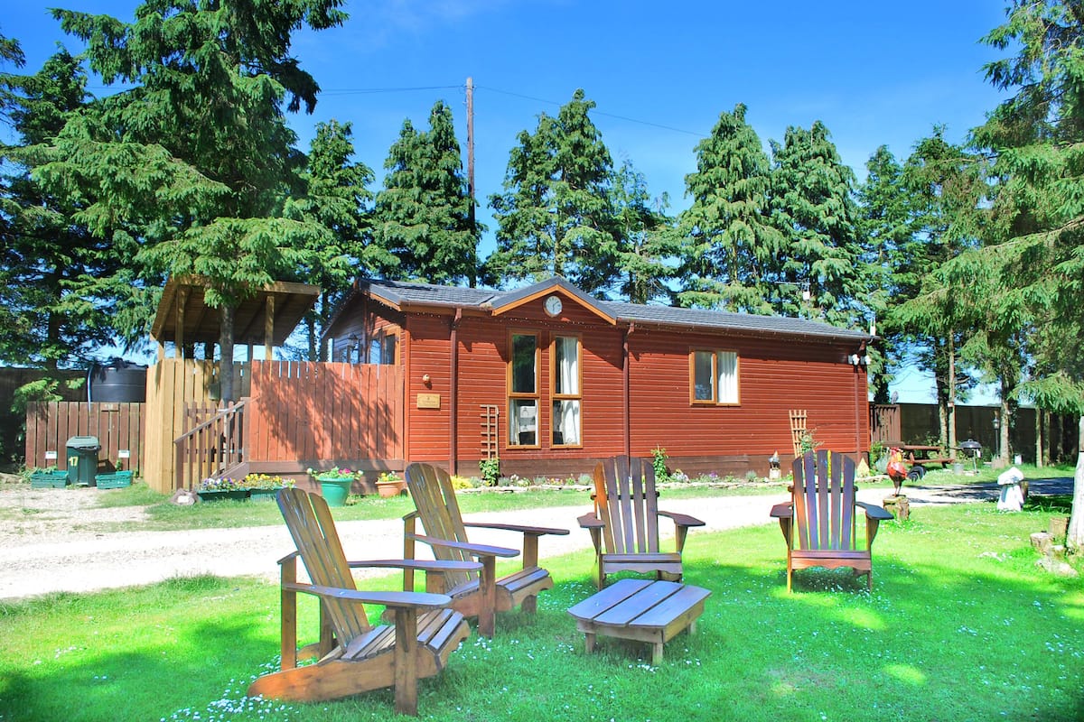 A cabin with a wooden deck, two Adirondack chairs, and a small table.
