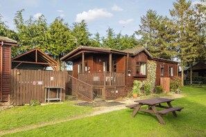 A wooden cabin with a porch, a picnic table, and a fenced area. - Rocklands Lodges (Pickering)