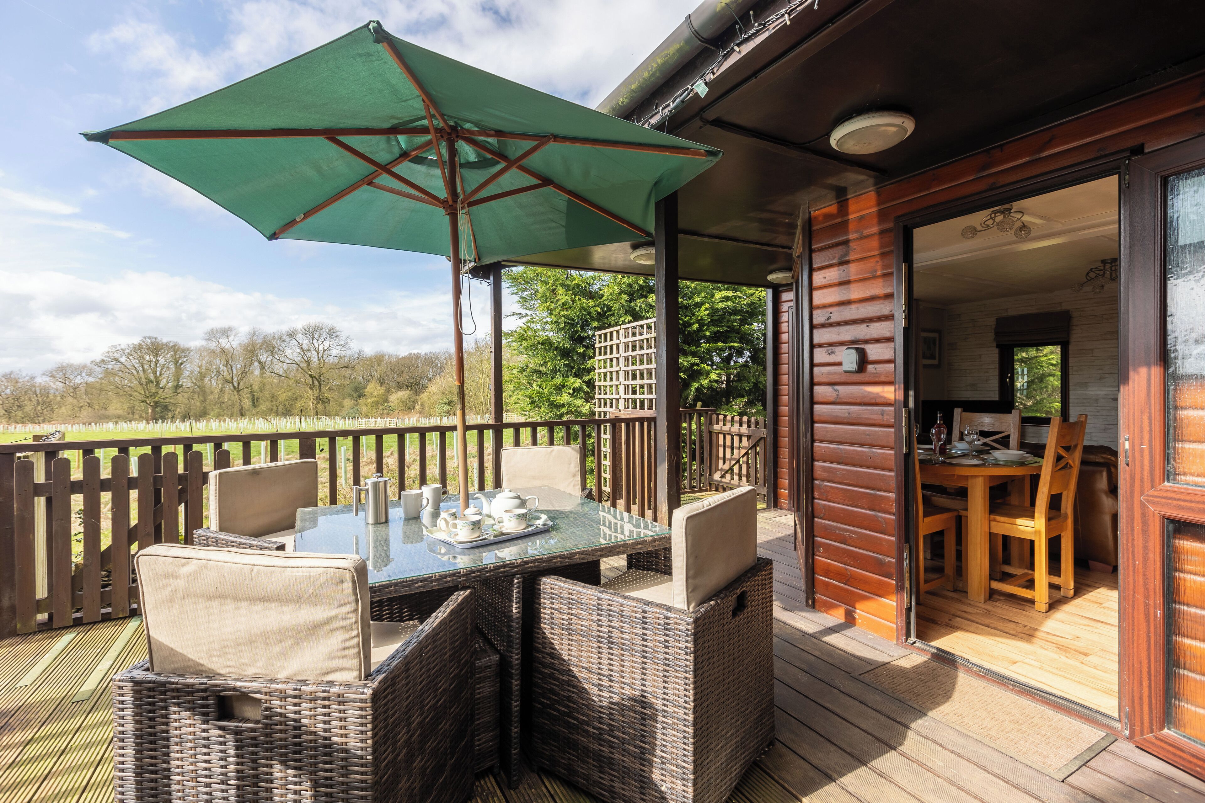 A covered outdoor dining area with wicker furniture and a green umbrella.