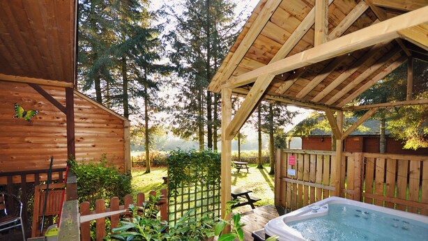 Una terraza de madera con un jacuzzi, una mesa de picnic y una valla de madera.