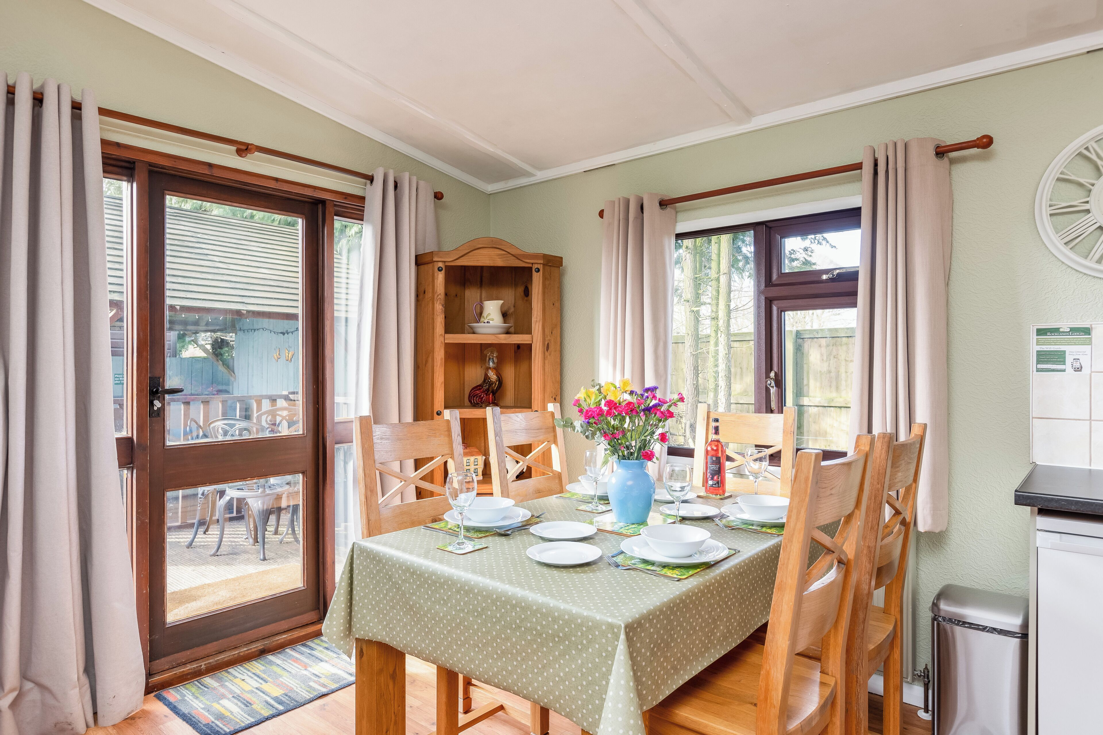 A dining area with a table set for four, wooden chairs, a vase with flowers, and a wooden cabinet with dishes.
