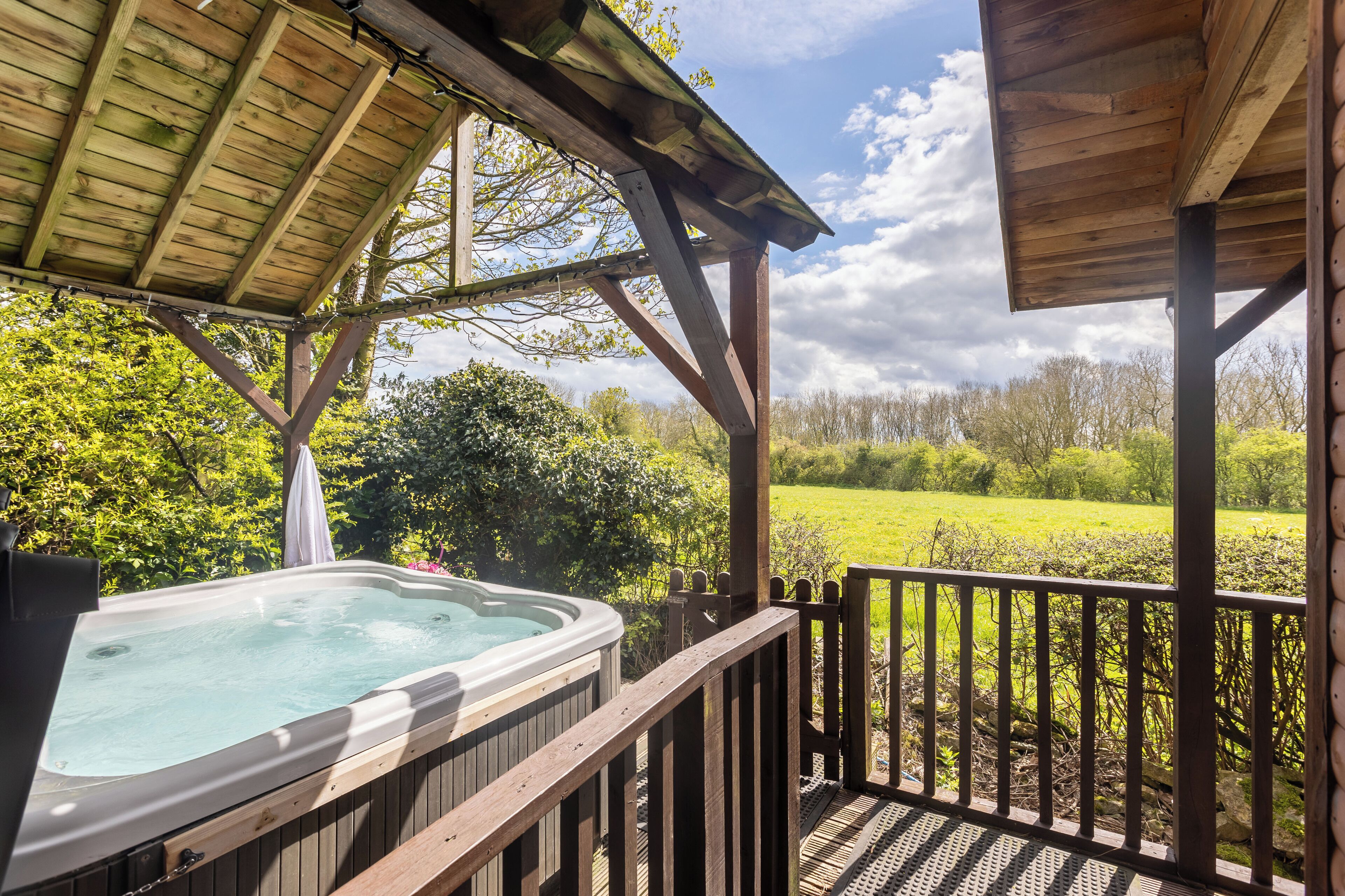 Ein Whirlpool auf einer Holzterrasse mit Blick auf ein grünes Feld und Bäume.