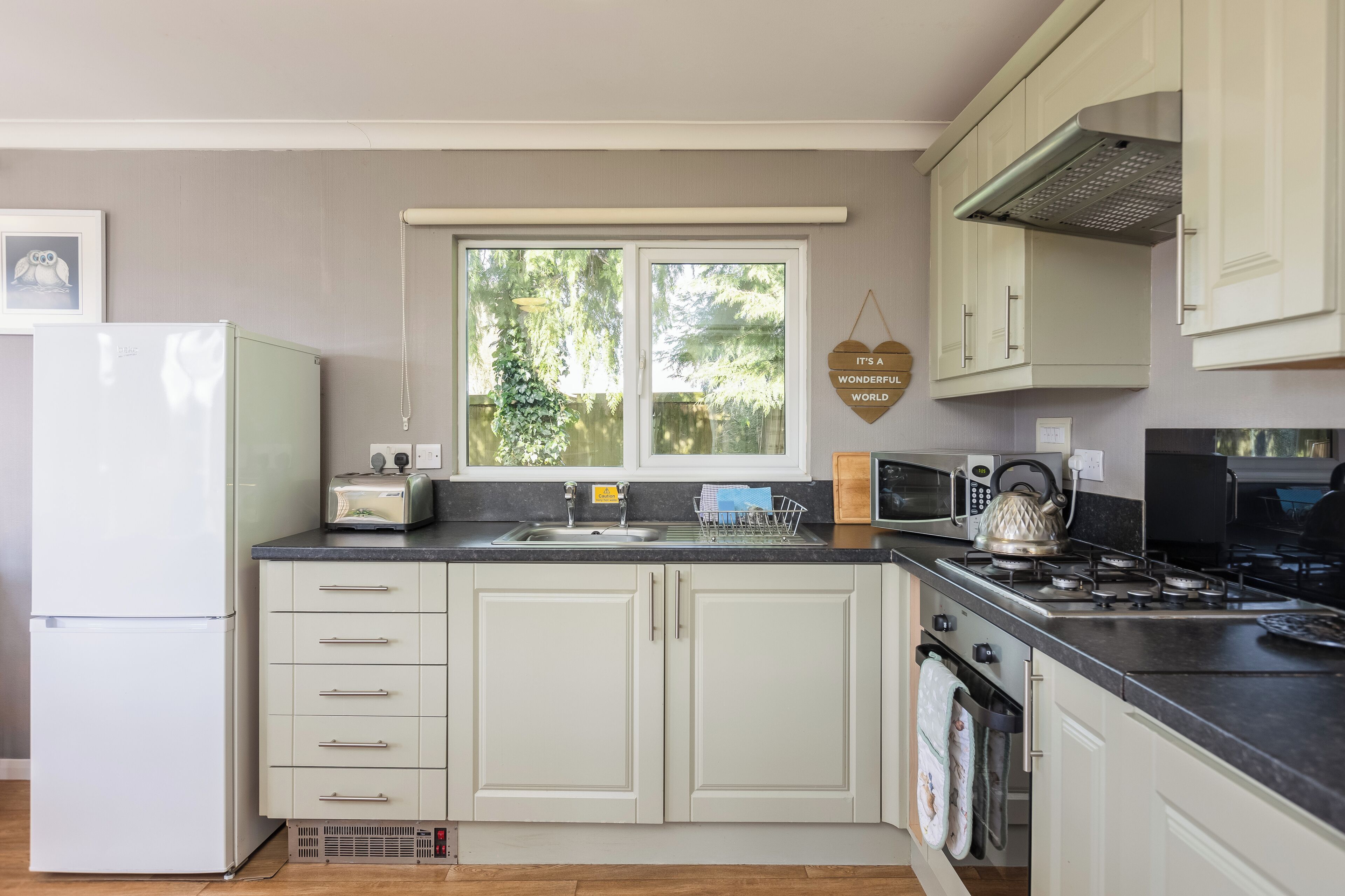 A kitchen with a refrigerator, toaster, sink, microwave, kettle, and stove.