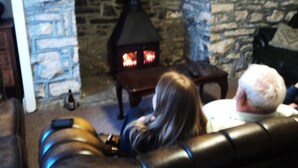 Una chimenea de piedra con un conducto negro, un sofá de cuero y una persona sentada en primer plano.