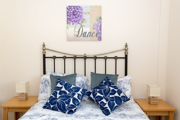 A bed with a floral-patterned bedspread, two matching pillows, and a wall-mounted artwork with the word "Dance".