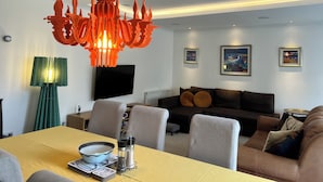 A modern living room with a dining area, a unique orange chandelier, a flat-screen TV, and framed artwork on the walls. - Crieff Armoury Luxury Self Catering Apartment (Crieff)