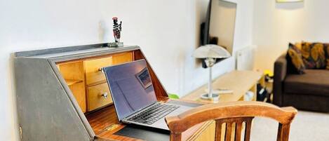 Ein Zimmer mit Laptop auf einem Schreibtisch, einem Sessel, einem Fernseher und einem Sofa.