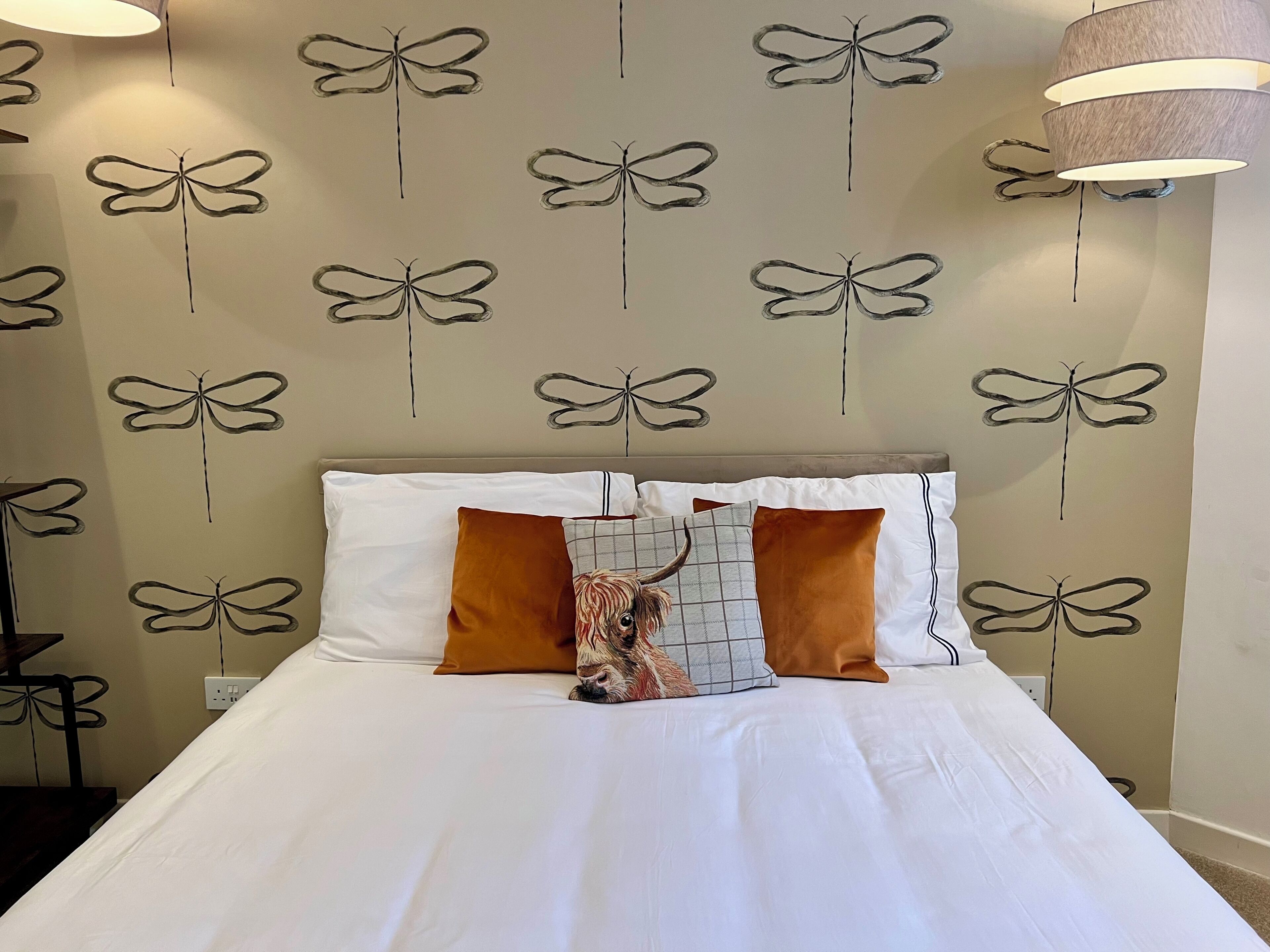 A bed with white bedding, two brown pillows, and a patterned throw.