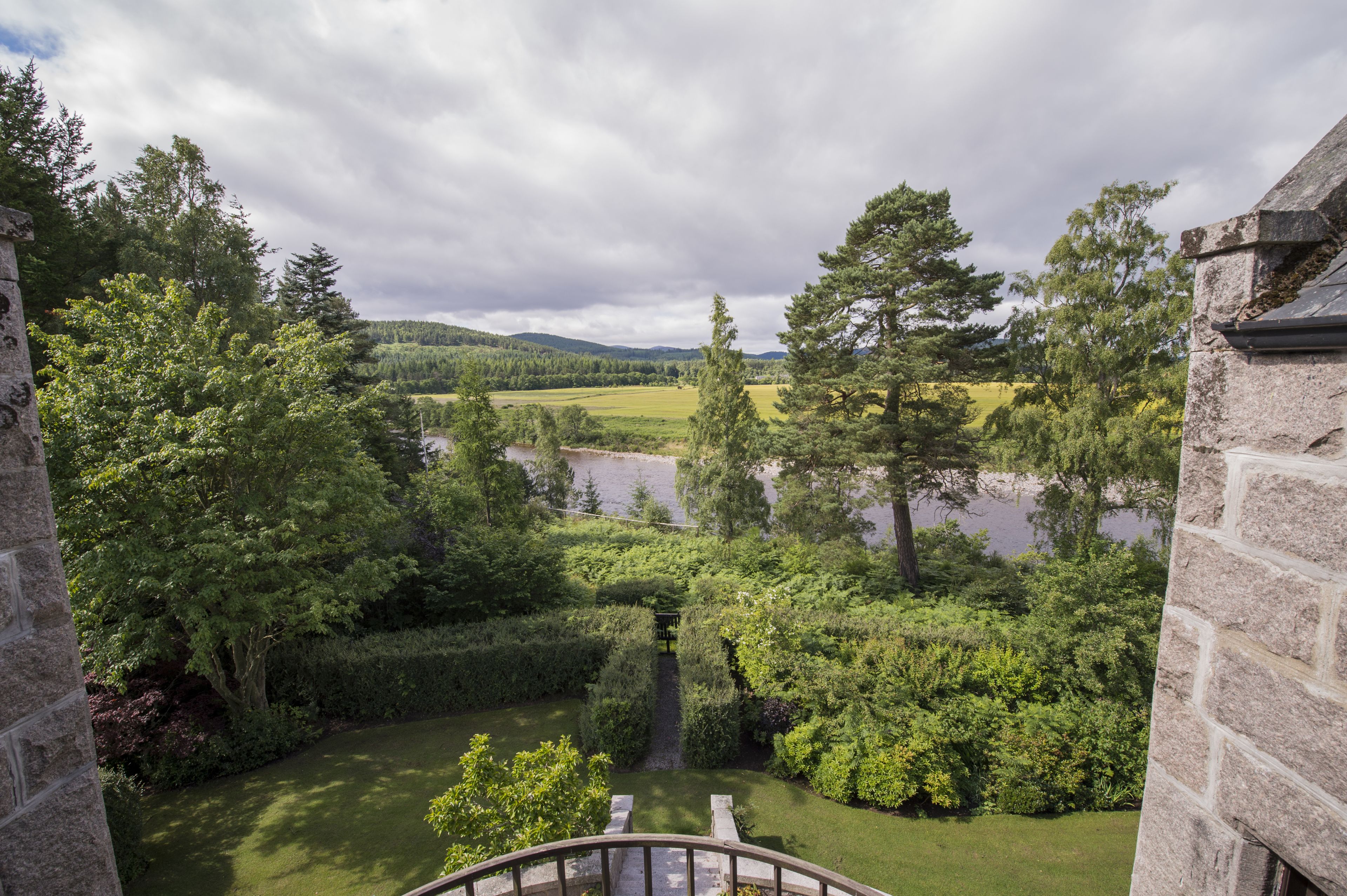 Un bâtiment en pierre offrant une vue sur un jardin luxuriant et une rivière.