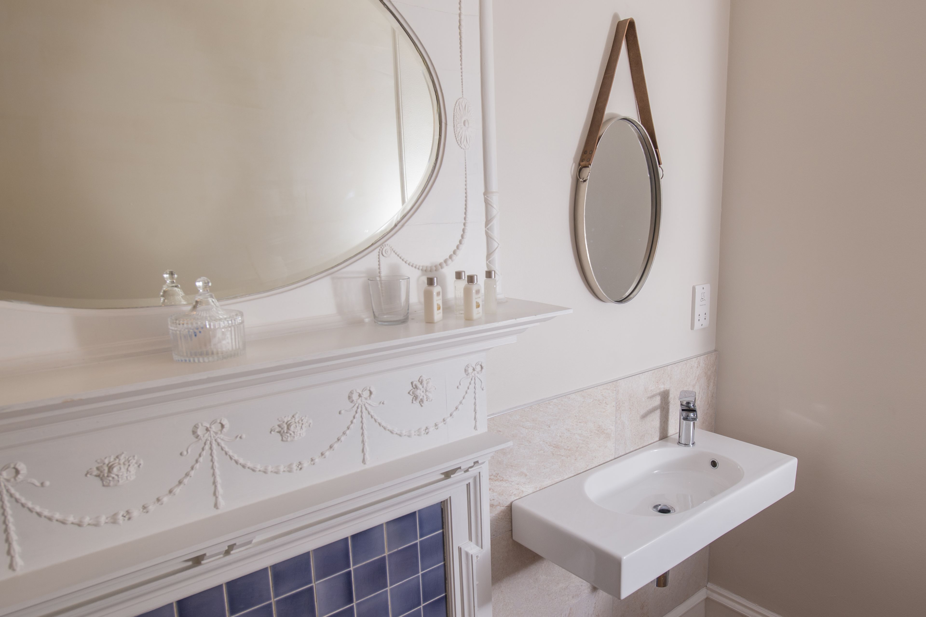Un baño con tocador blanco, un espejo grande, un lavamanos y un panel decorativo en la pared.