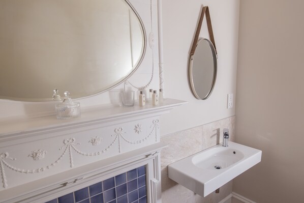 A bathroom with a white vanity, a large mirror, a sink, and a decorative wall panel. - Lys-Na-Greyne Country House (Aboyne)
