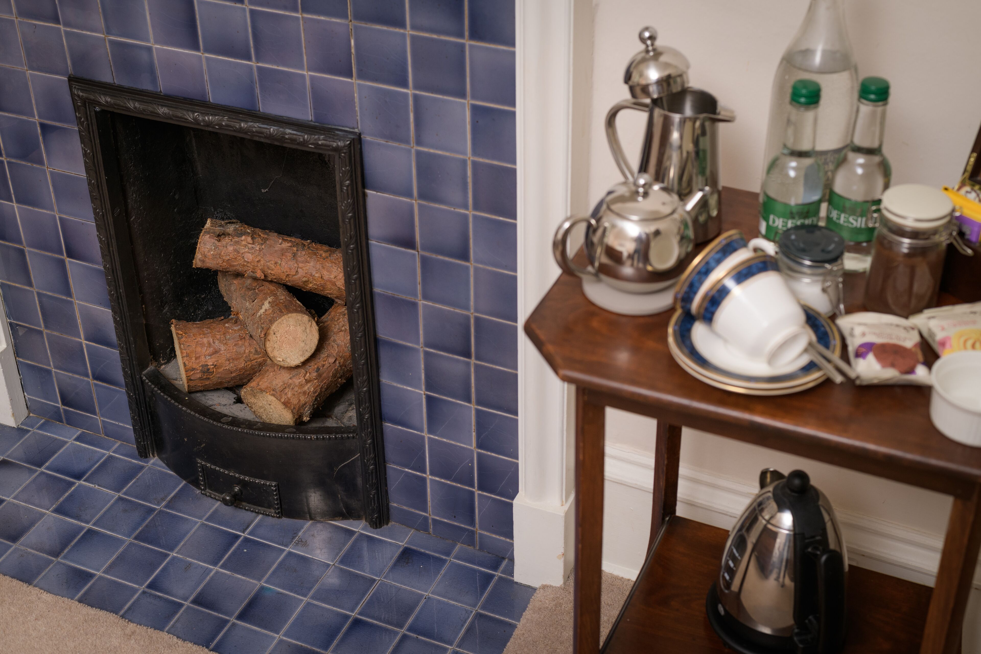 A fireplace with logs, a table with kitchenware, and a kettle.