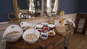 A breakfast buffet with various cereals, fruits, and bread on a wooden table in a room with blue walls and a large mirror. - Lys-Na-Greyne Country House (Aboyne)