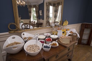 Un bufé de desayuno con diversos cereales, frutas y pan sobre una mesa de madera en una habitación con paredes azules y un espejo grande.
