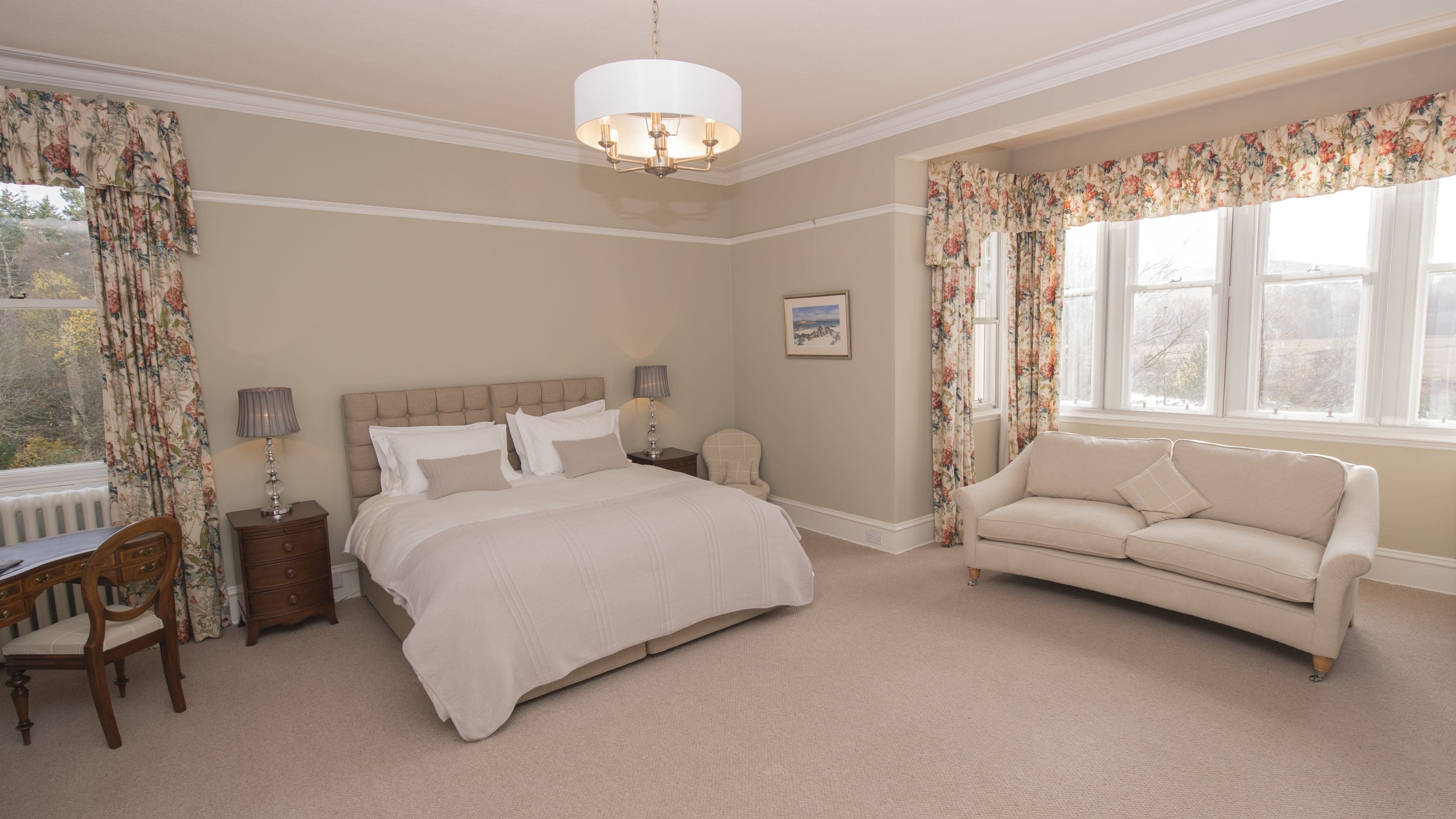 A bedroom with a large bed, a sitting area with a sofa, a desk, and a chair.
