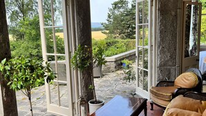 A room with a large window, a wooden bench, a sofa, and potted plants. - Lys-Na-Greyne Country House (Aboyne)