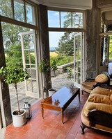 Una habitación con un ventanal grande, un banco de madera, un sofá y plantas en macetas.