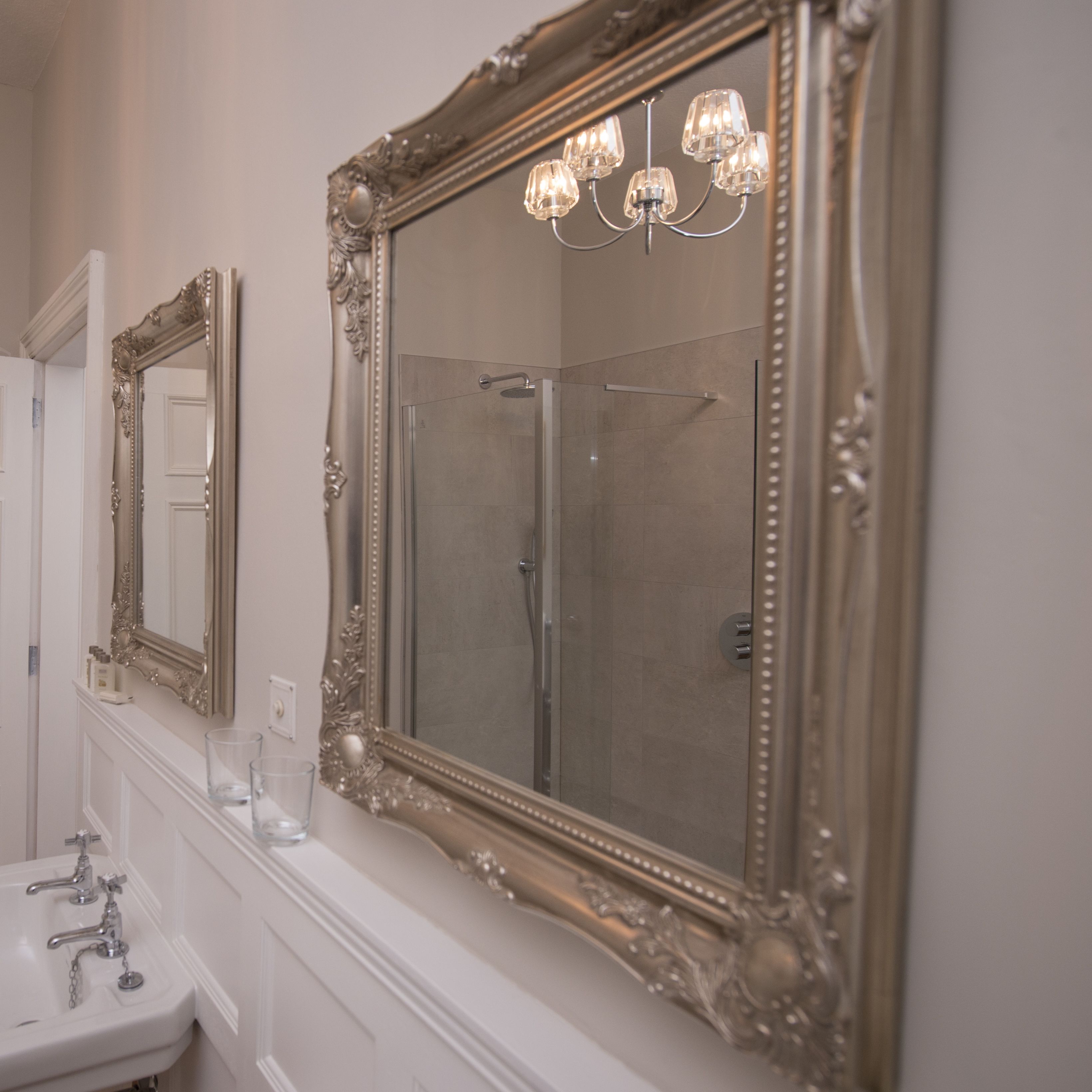 Un baño con dos espejos decorativos, un lavamanos y una ducha.