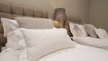 A neatly made bed with white linens and pillows, a tufted headboard, and a bedside lamp.