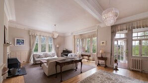 A spacious living room with a fireplace, a large rug, and a view of the garden through the windows. - Lys-Na-Greyne Country House (Aboyne)