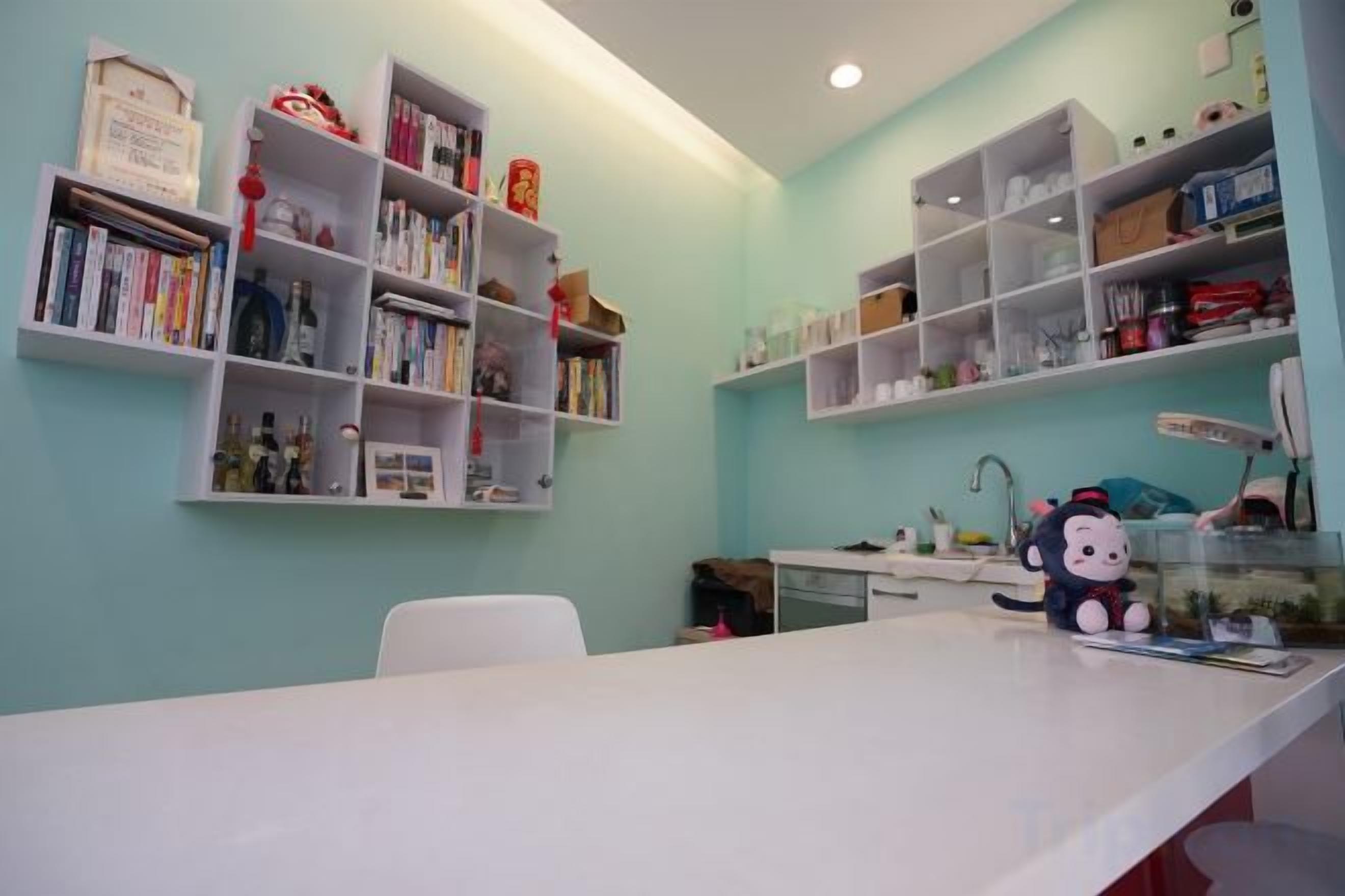 Una stanza con una scrivania bianca, mensole piene di libri e oggetti decorativi, un tavolino con un peluche Hello Kitty e una sedia bianca.