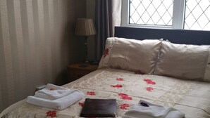 A neatly made bed with floral bedding, a bedside lamp, and a window with a metal grill. - Thurlestone Guest House (St Ives)