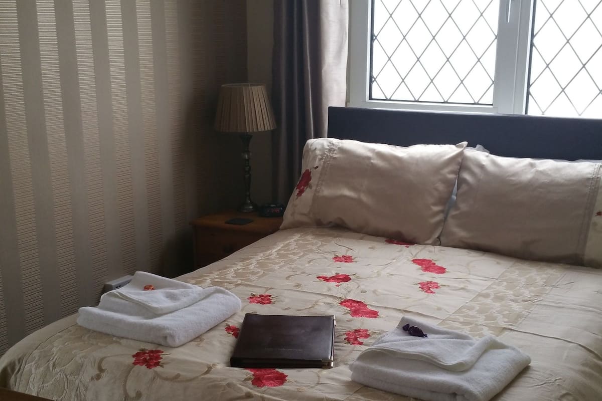 A neatly made bed with floral bedding, a bedside lamp, and a window with a metal grill.