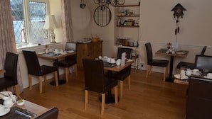 A dining area with wooden tables and chairs, a chandelier, and shelves with kitchen items. - Thurlestone Guest House (St Ives)