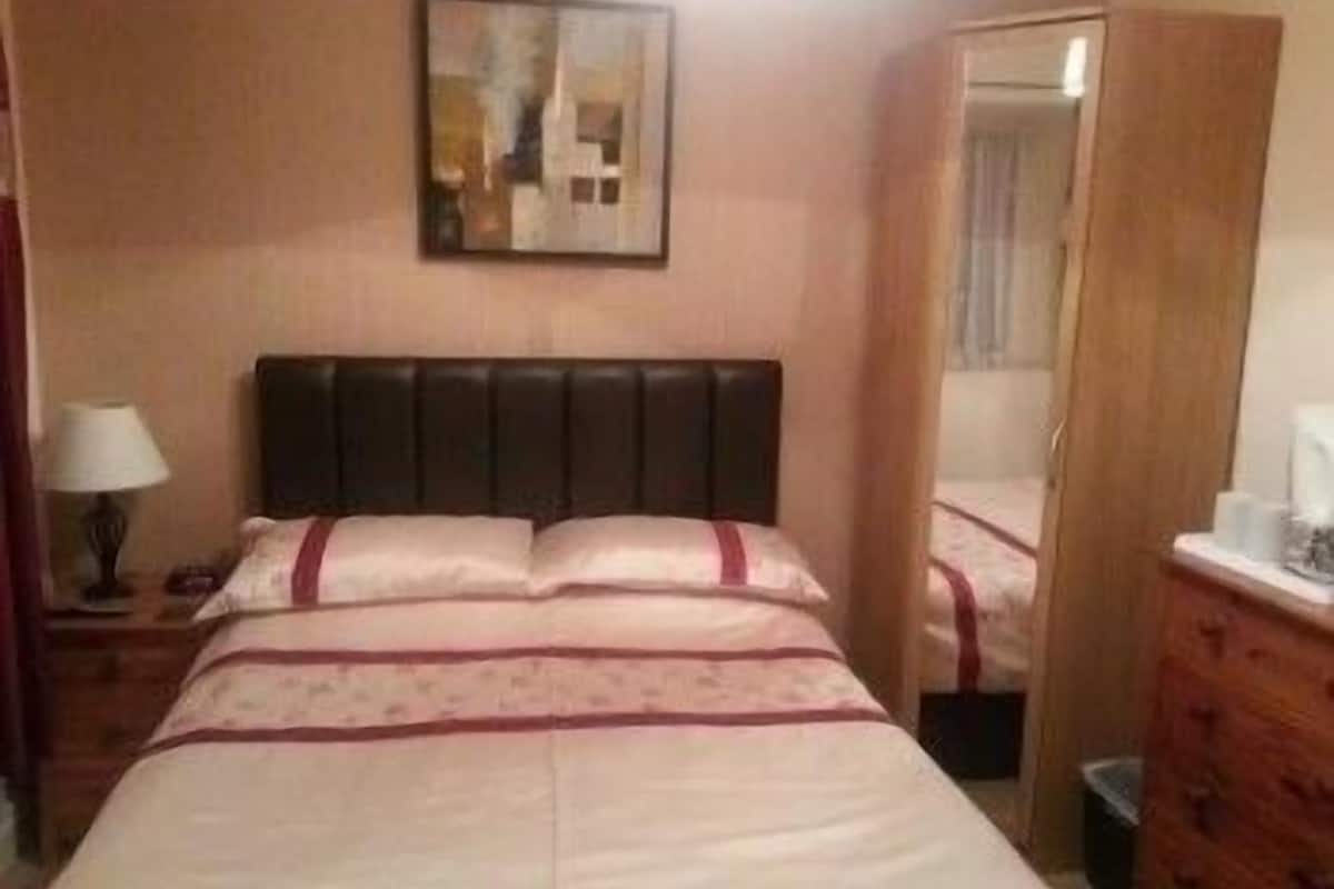 A hotel room with a bed, a nightstand, a lamp, a mirror, and a wooden dresser.