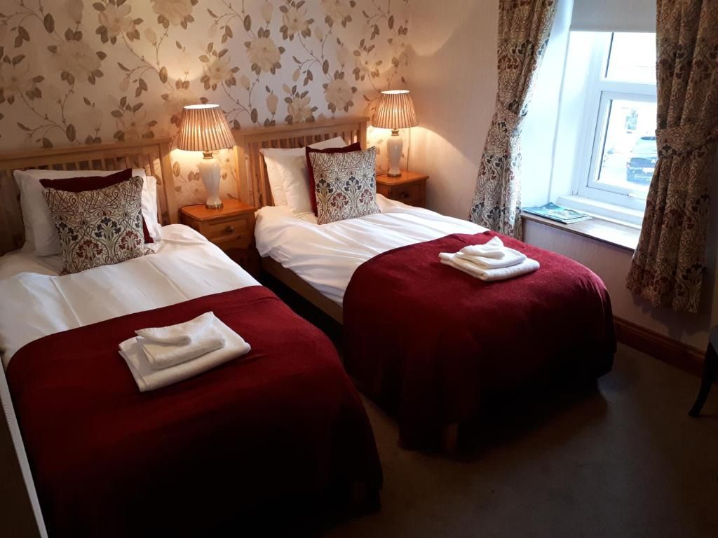 Een hotelkamer met twee bedden, elk voorzien van een rode sprei en witte lakens, met nachtkastjes met lampen ernaast.
