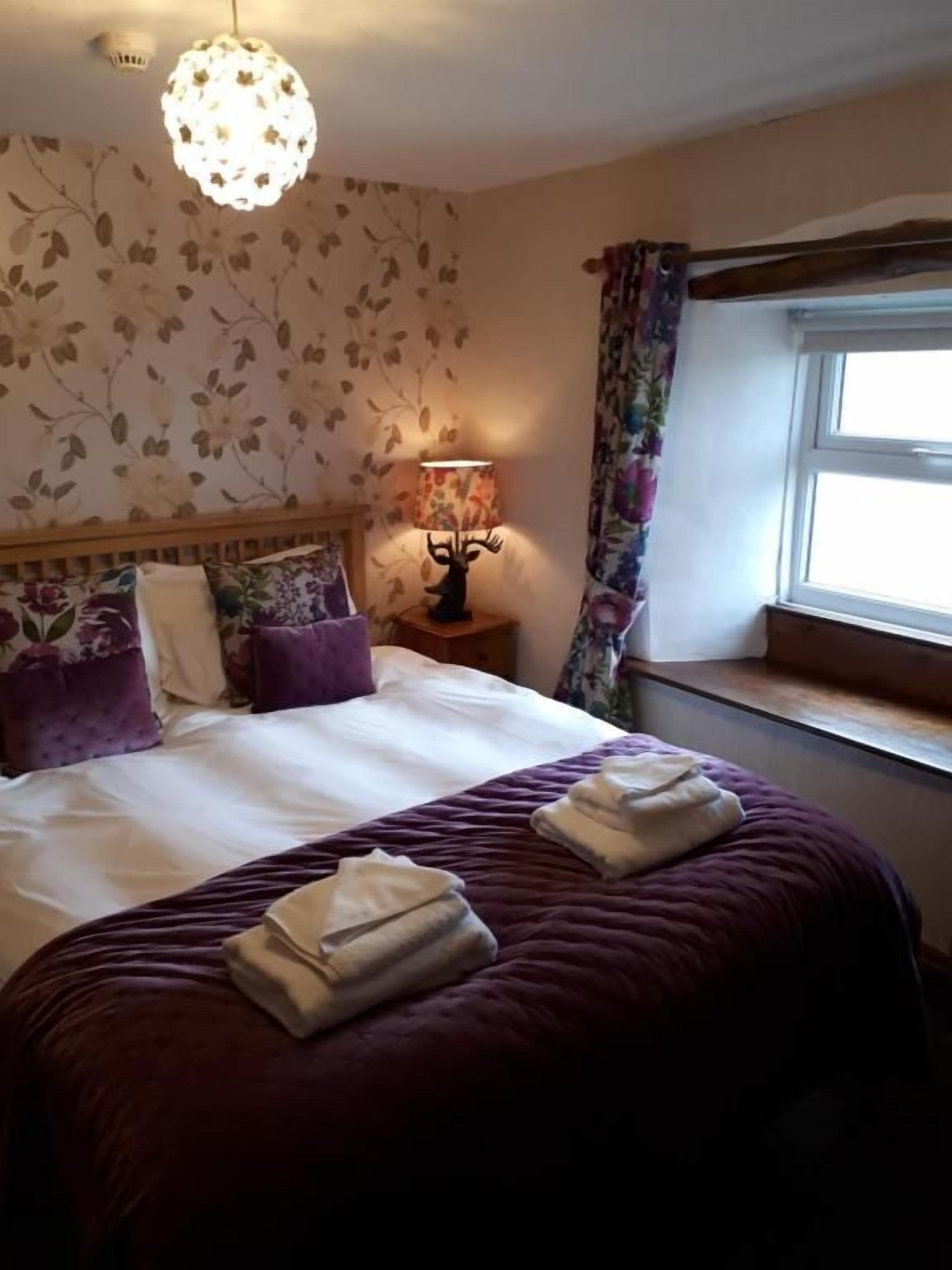 A hotel room with a bed, a nightstand, a lamp, and a window with curtains.