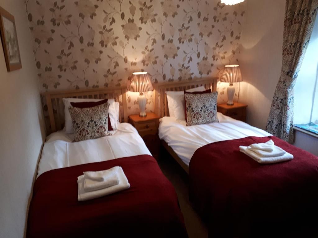 Une chambre d’hôtel avec deux lits, chacun recouvert d’une couverture rouge et doté de draps blancs, et de chaque côté, une table de chevet avec une lampe.