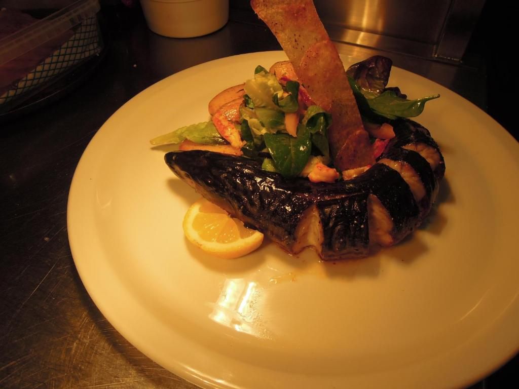 A plate with grilled fish, vegetables, and a lemon wedge.