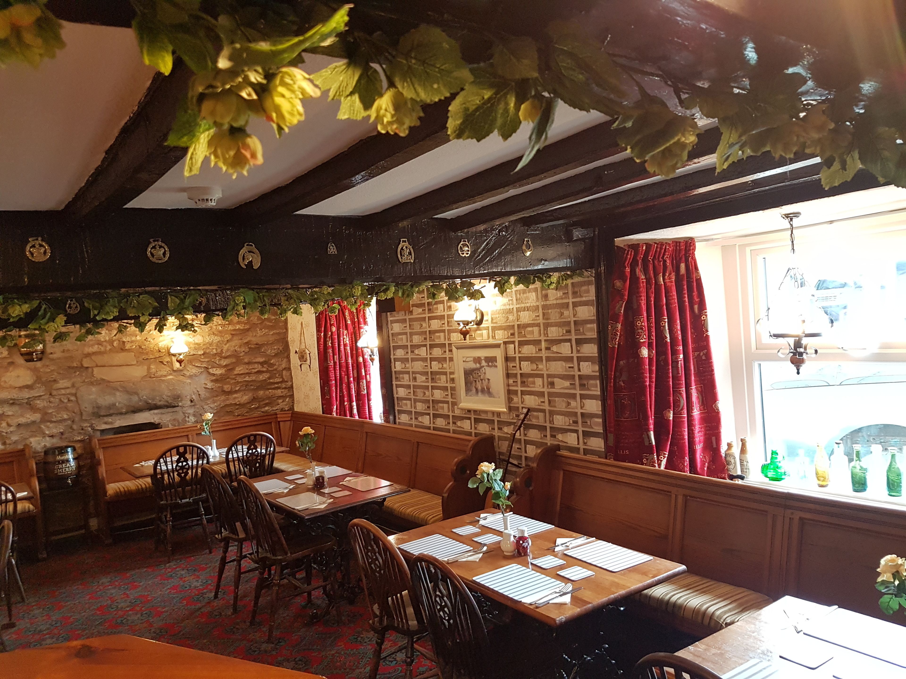 A cozy dining area with wooden tables and benches, stone walls, and red curtains.