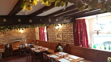 A cozy dining area with wooden tables and benches, stone walls, and red curtains.