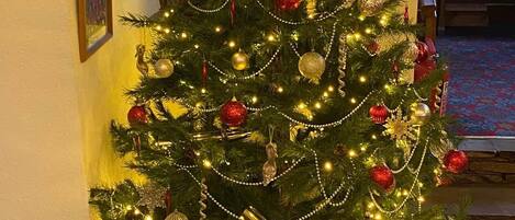 Un árbol de Navidad decorado con luces y adornos, ubicado en una esquina con una ventana y cuadros en la pared.
