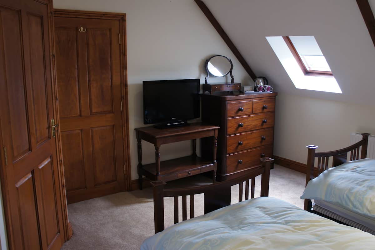 A bedroom with a wooden desk, a television, a dresser, and two beds.