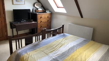 A bedroom with a bed, a desk, a dresser, a television, and a skylight.