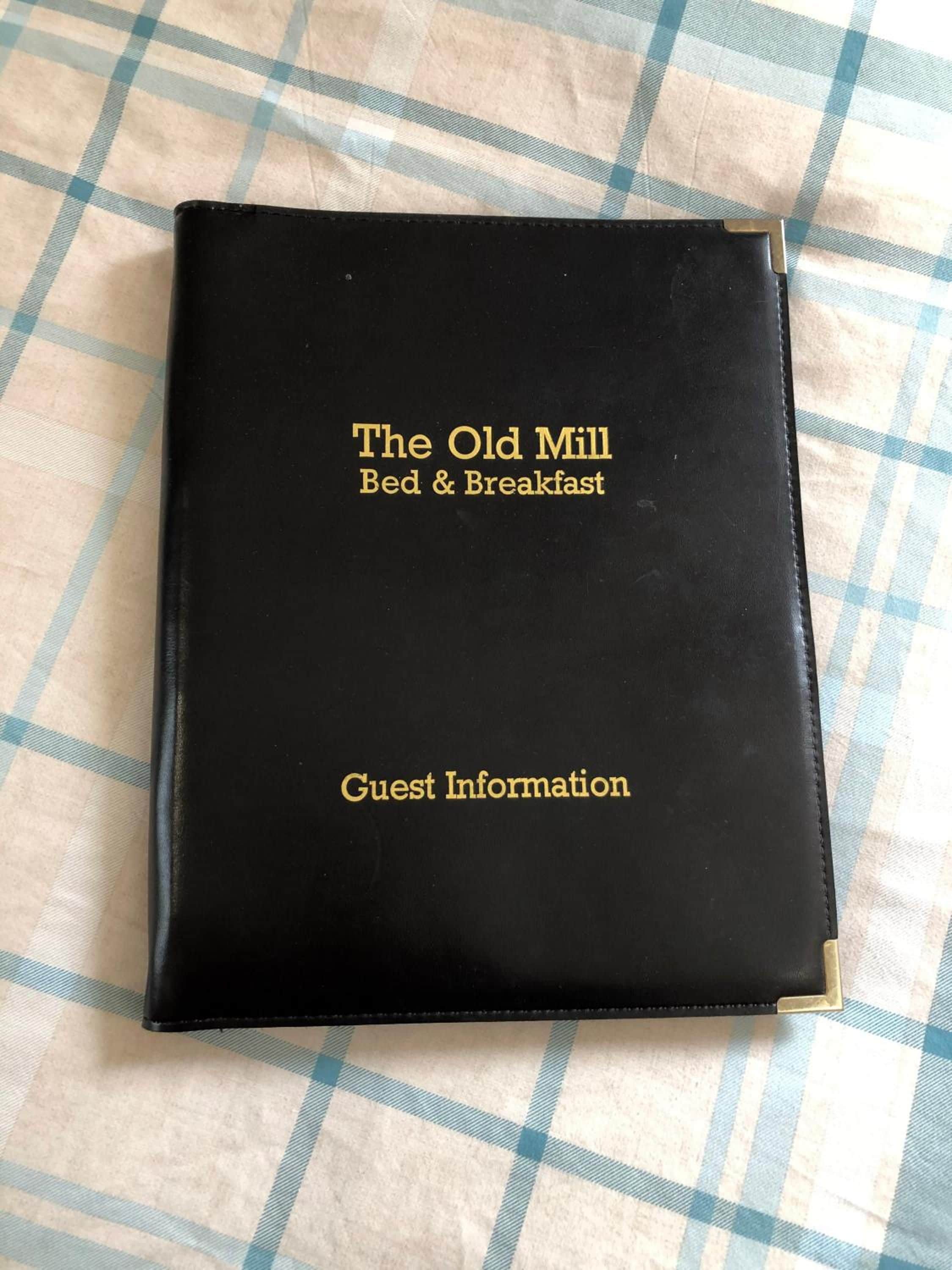 Un libro negro con el título 'The Old Mill Bed & Breakfast' y la frase 'Guest Information' escrita en la portada.