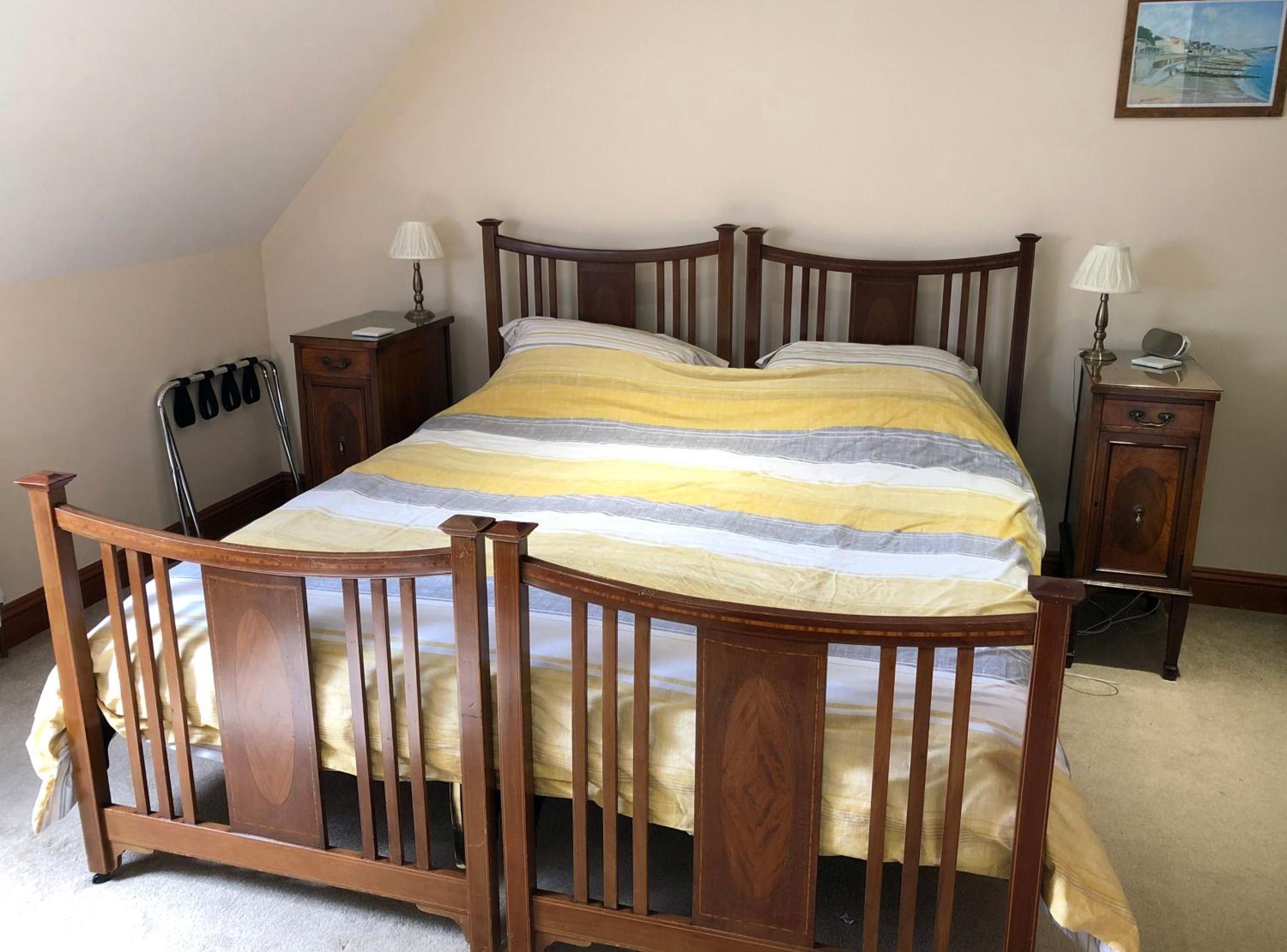 A bedroom with a wooden four-poster bed, two bedside tables, a nightstand, and a chair.
