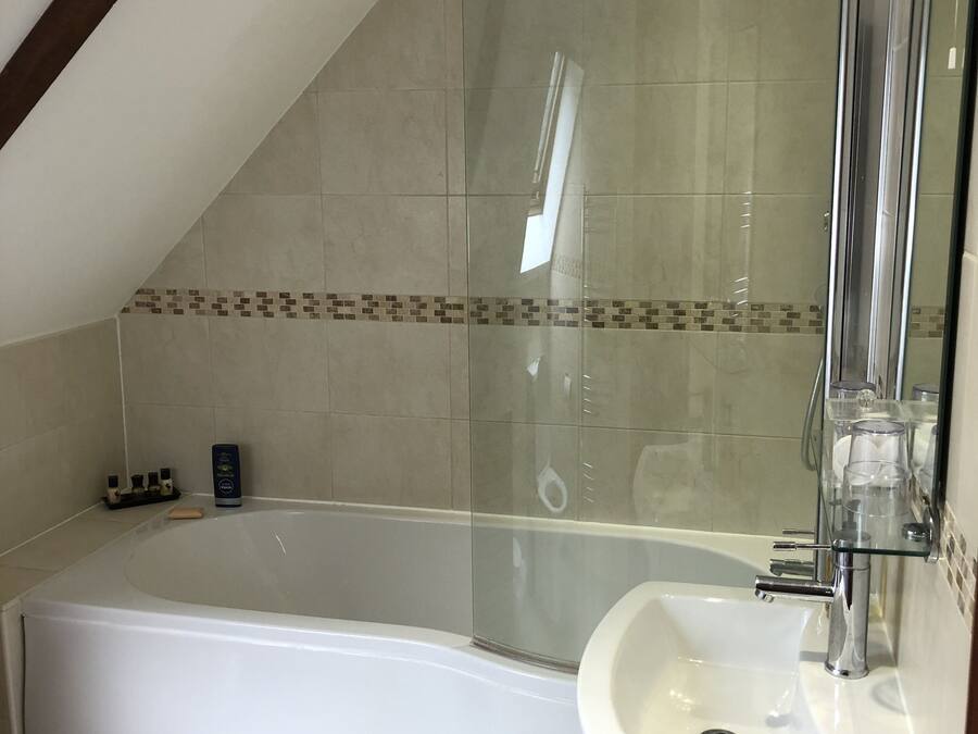 A corner bathroom with a glass-enclosed shower, a white bathtub, and a sink with a glass shelf.