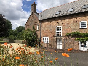 A brick building with multiple windows and a door, surrounded by a garden with orange flowers. - The Old Mill Bere Regis (Wareham)