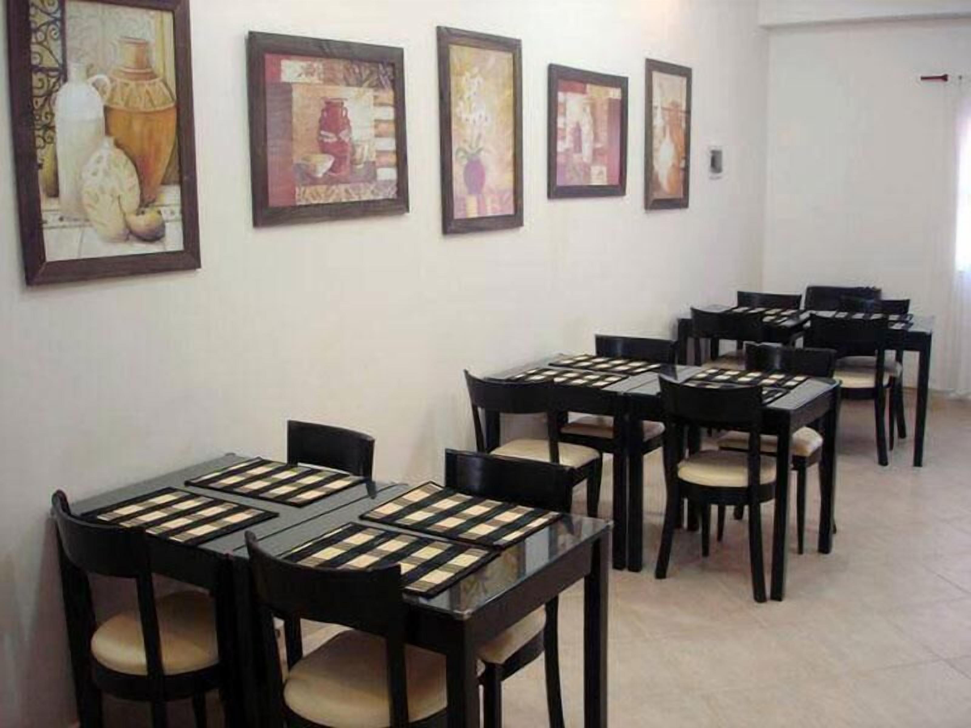 A dining area with multiple tables and chairs, framed artwork on the walls, and a tiled floor.