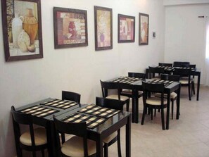 A dining area with multiple tables and chairs, framed artwork on the walls, and a tiled floor.
