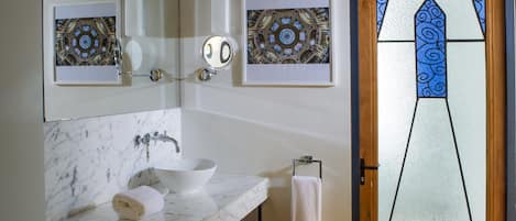 Un baño con lavamanos de mármol, un espejo y dos vidrieras enmarcadas.