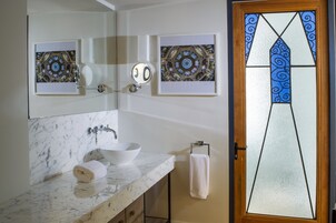 Un baño con lavamanos de mármol, un espejo y dos vidrieras enmarcadas.