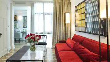 A modern living room with a red sofa, a glass coffee table with a vase of flowers, and a dining area in the background.